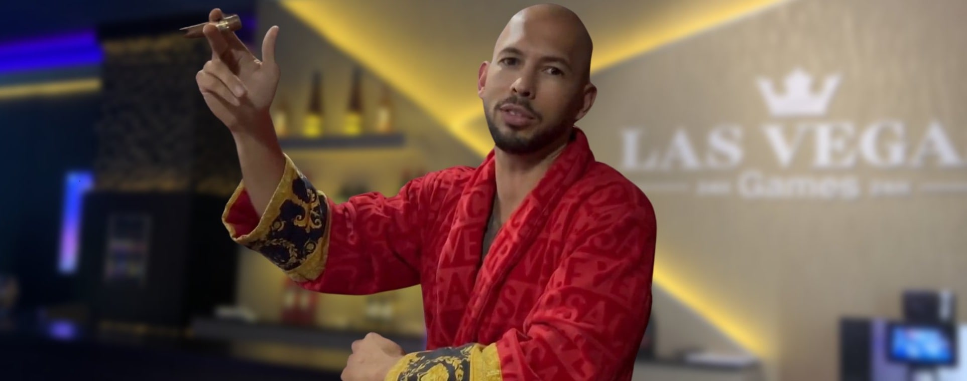 A Andrew Tate in a red patterned robe holding a cigar inside a luxurious casino setting with 'Las Vegas Games' signage in the background.